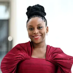 Chimamanda Ngozi Adichie, una de las escritoras inglesas actuales más influyentes, sonríe con un vestido rojo plisado.