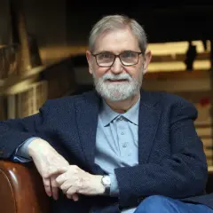 Un hombre mayor con gafas y barba blanca, vestido con chaqueta y polo, evoca la figura de escritores catalanes del siglo XX.