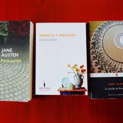 Tres de los mejores libros de Jane Austen: Persuasión, Orgullo y Prejuicio y La abadía de Northanger, dispuestos sobre una mesa de madera.