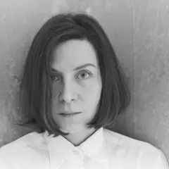Retrato en blanco y negro de Donna Tart, con su mirada intensa y cabello corto, vestida con una camisa blanca.