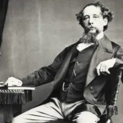 Charles Dickens, autor de libros famosos, posa con una estatua y un libro a su lado.