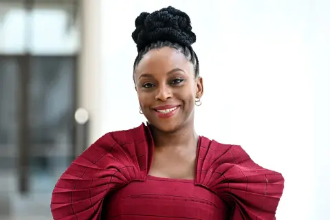 Chimamanda Ngozi Adichie, una de las escritoras inglesas actuales más influyentes, sonríe con un vestido rojo plisado.