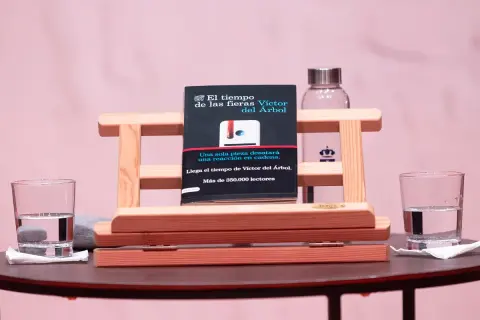 Libro "El tiempo de las fieras" de Víctor del Árbol, con dos vasos de agua y un fondo rosa.