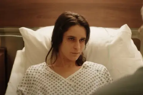 Una mujer en bata de hospital mira fijamente, quizás buscando respuestas sobre el hombre del laberinto final explicado.