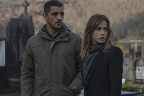 Un hombre y una mujer en un cementerio, con aspecto preocupado. Podría ser una escena del resumen de "Ofrenda a la tormenta".