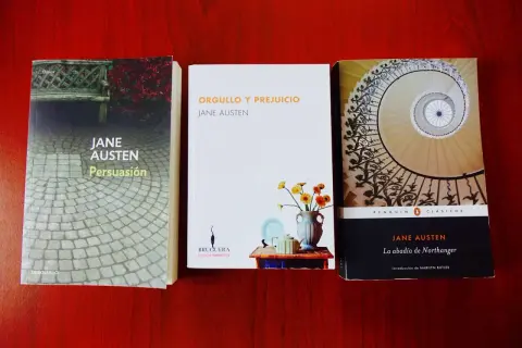 Tres de los mejores libros de Jane Austen: Persuasión, Orgullo y Prejuicio y La abadía de Northanger, dispuestos sobre una mesa de madera.