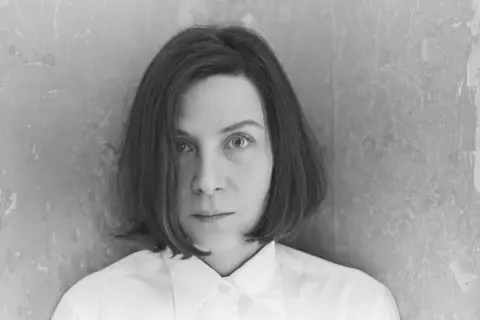 Retrato en blanco y negro de Donna Tart, con su mirada intensa y cabello corto, vestida con una camisa blanca.