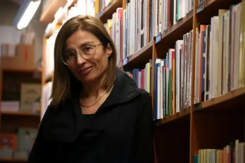 Una mujer con gafas sonríe entre estanterías llenas de libros, evocando la rica tradición de las escritoras catalanas famosas.
