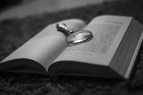 Un libro aperto con una lente d'ingrandimento posata sulle pagine, evocando un'atmosfera di mistero e segreti domestici, un vero domestic noir.