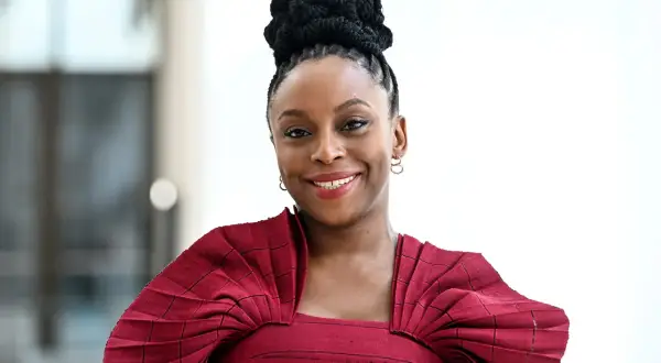 Chimamanda Ngozi Adichie, una de las escritoras inglesas actuales más influyentes, sonríe con un vestido rojo plisado.