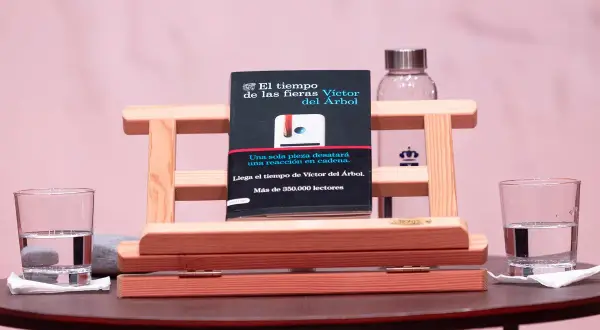 Libro "El tiempo de las fieras" de Víctor del Árbol, con dos vasos de agua y un fondo rosa.
