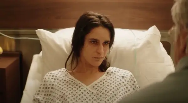 Una mujer en bata de hospital mira fijamente, quizás buscando respuestas sobre el hombre del laberinto final explicado.