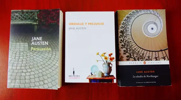 Tres de los mejores libros de Jane Austen: Persuasión, Orgullo y Prejuicio y La abadía de Northanger, dispuestos sobre una mesa de madera.