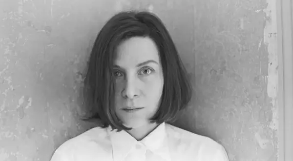 Retrato en blanco y negro de Donna Tart, con su mirada intensa y cabello corto, vestida con una camisa blanca.