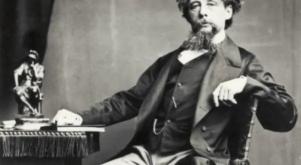 Charles Dickens, autor de libros famosos, posa con una estatua y un libro a su lado.