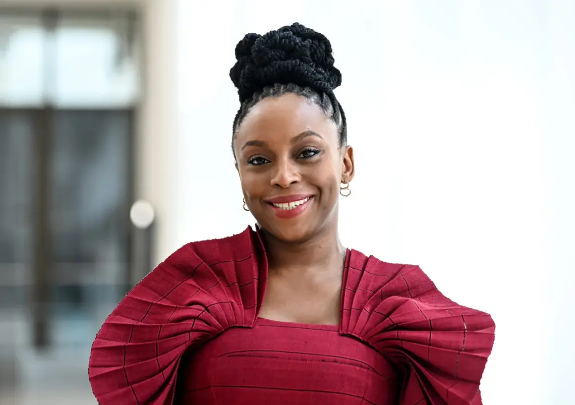 Chimamanda Ngozi Adichie, una de las escritoras inglesas actuales más influyentes, sonríe con un vestido rojo plisado.