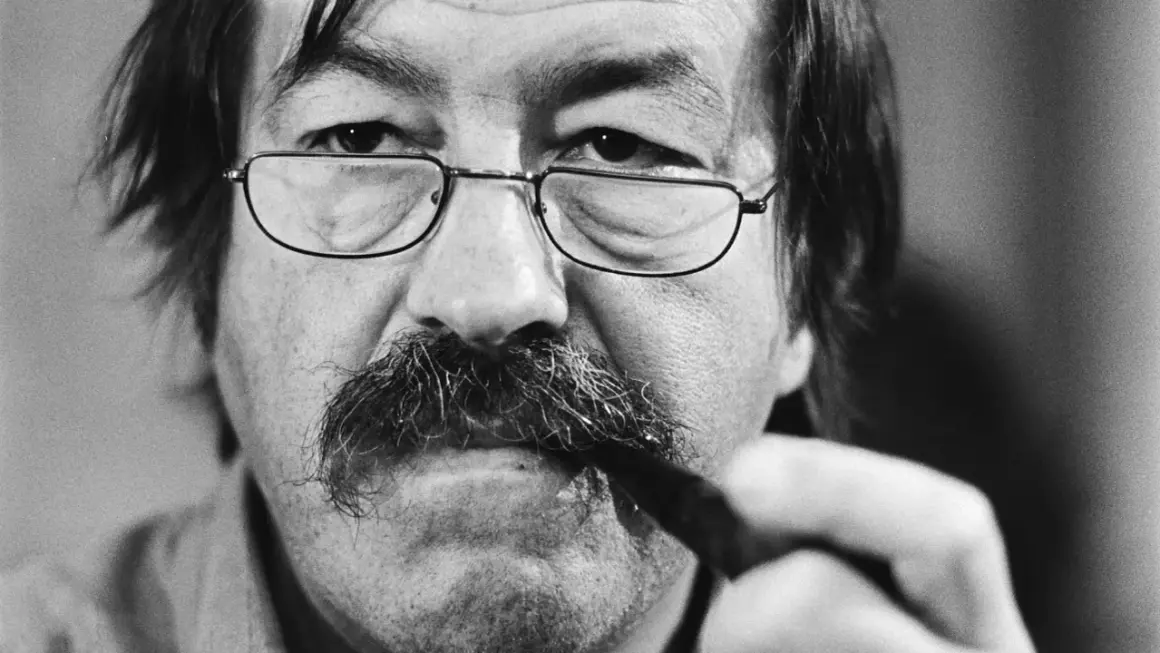 Primer plano de un hombre con gafas y bigote tupido, sosteniendo un bolígrafo. Podría ser uno de los escritores alemanes actuales.