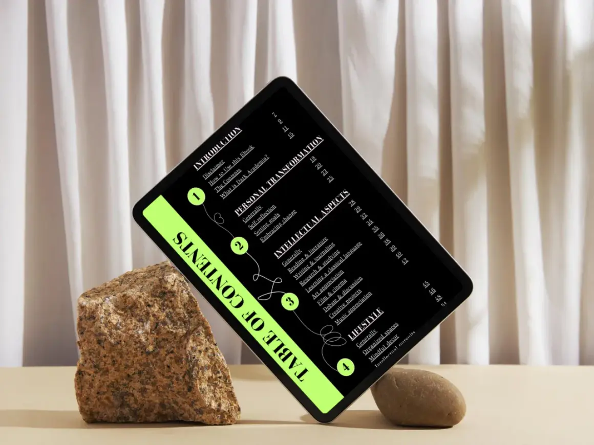 Una tablet muestra un índice de contenidos con un estilo "dark academia", rodeada de rocas y cortinas.