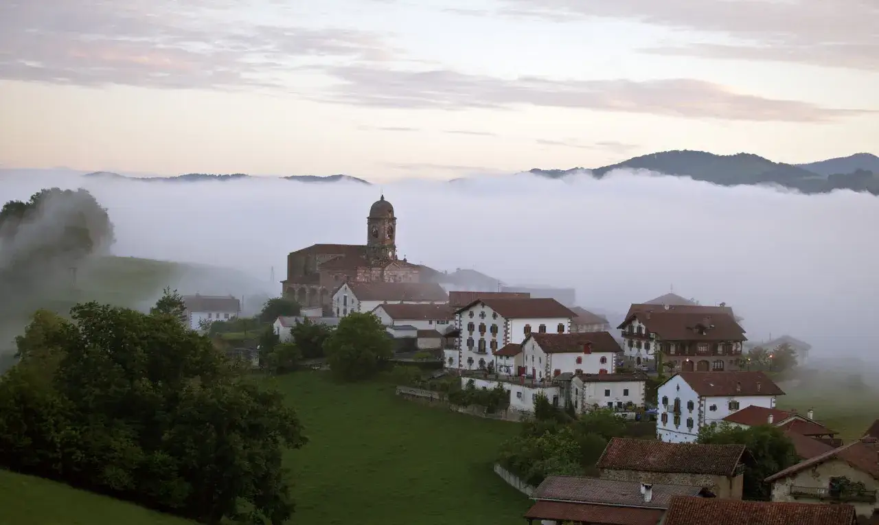 Pueblo vasco envuelto en niebla matutina, con una iglesia imponente. Un resumen visual de la 