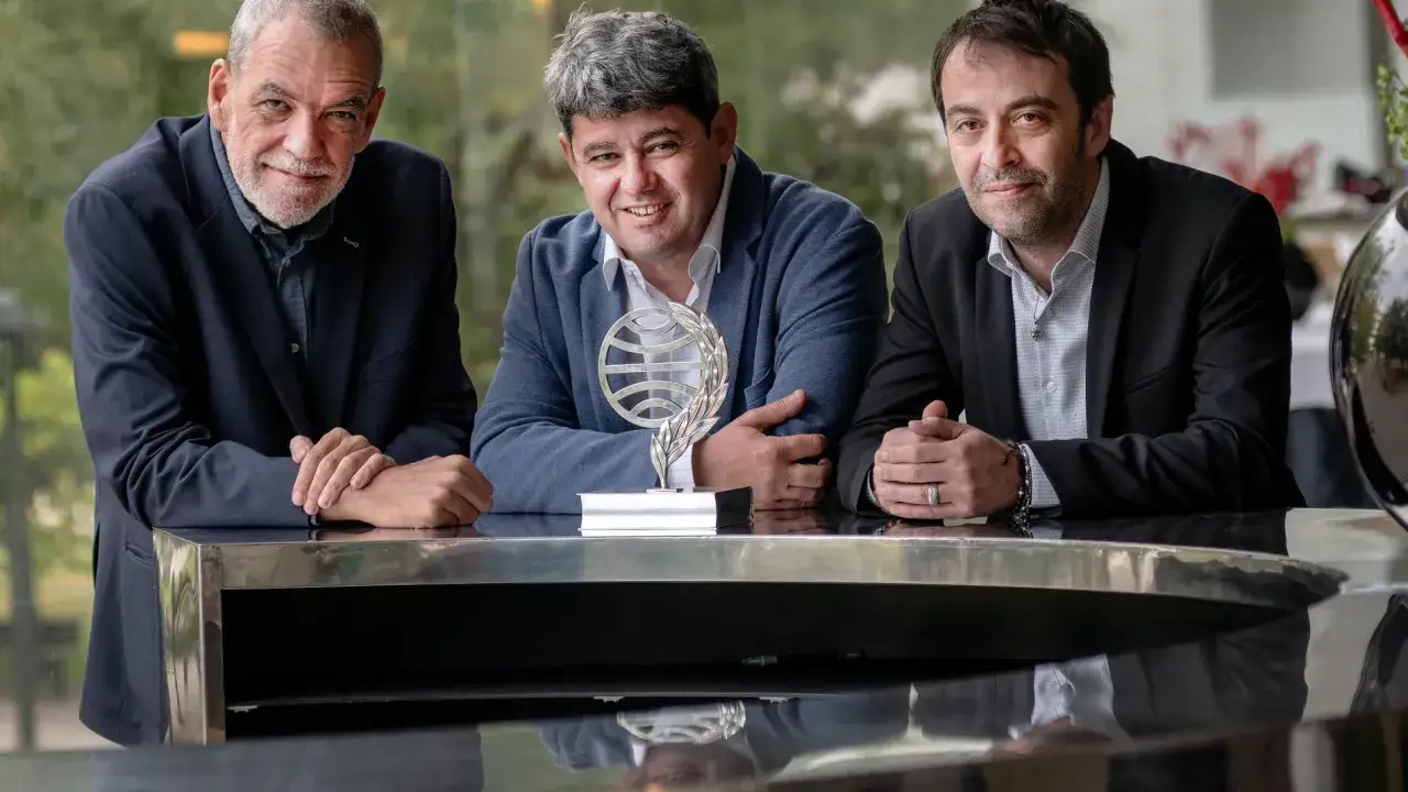 Tres hombres posan con un trofeo. Uno de ellos, con chaqueta azul, sonr&iacute;e. &iquest;Qui&eacute;n es Carmen Mola?
