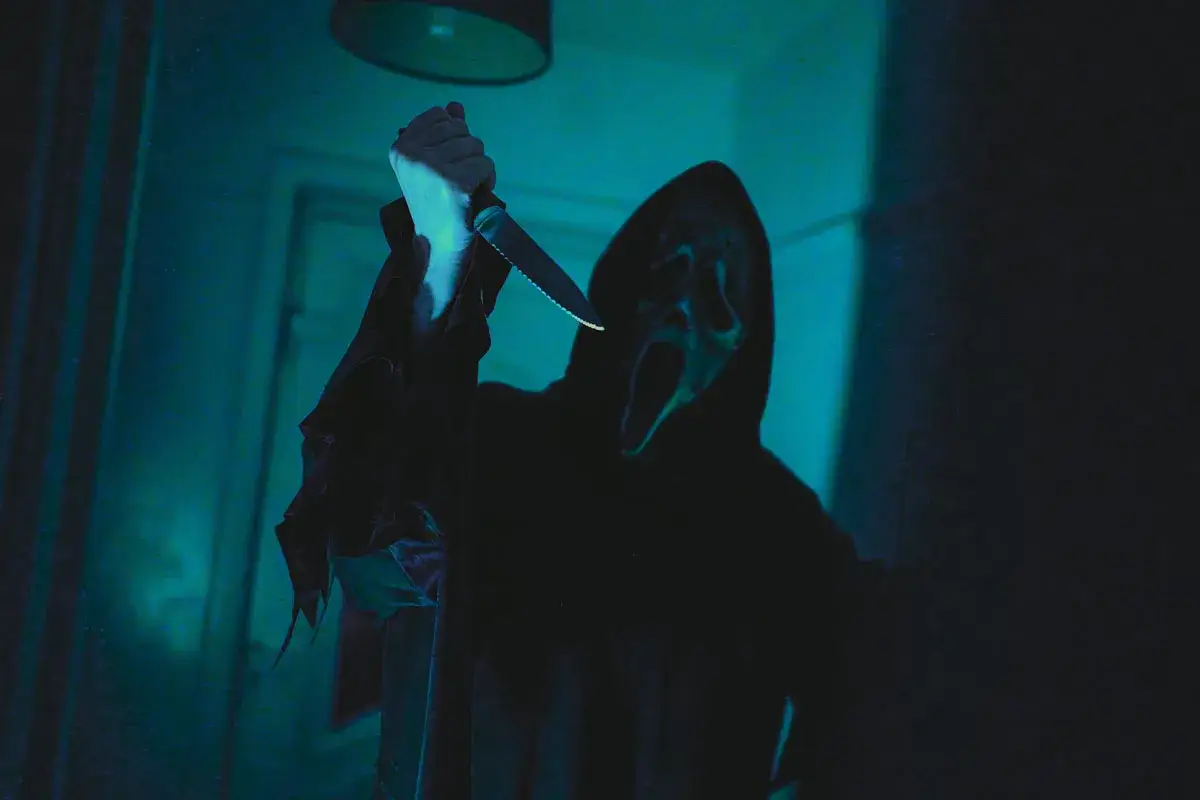 Figura enmascarada con cuchillo, envuelta en sombras y luz azul, evoca terror psicol&oacute;gico.
