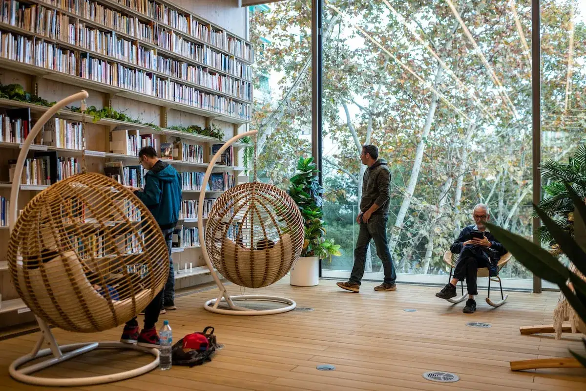 Gente en una biblioteca moderna, rodeada de estanterías llenas de libros, quizás buscando inspiración para los 100 libros que leer antes de morir.