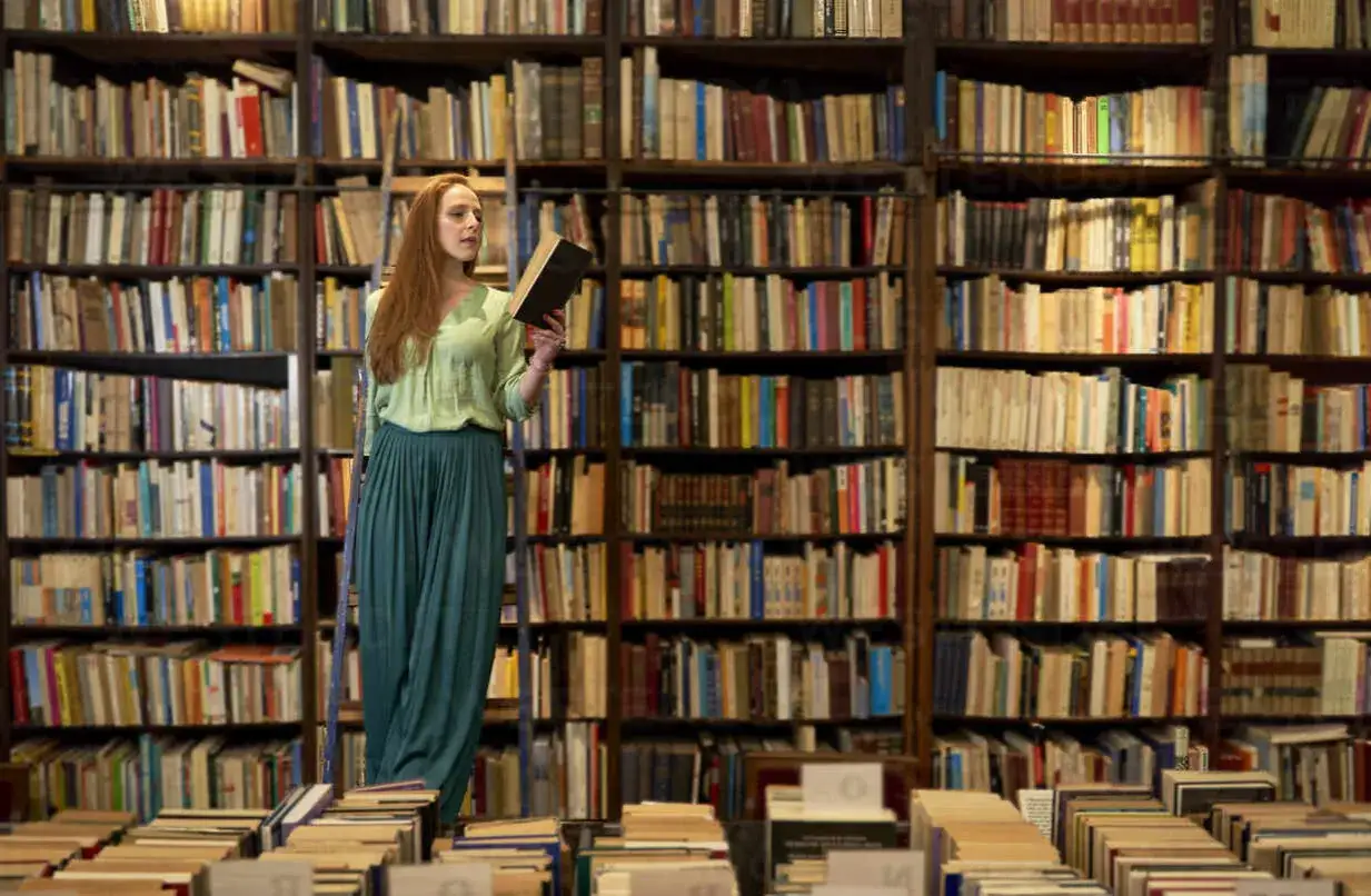 Mujer pelirroja en librería, rodeada de estanterías llenas de libros. Busca entre los libros recomendados para mujeres su próxima lectura.
