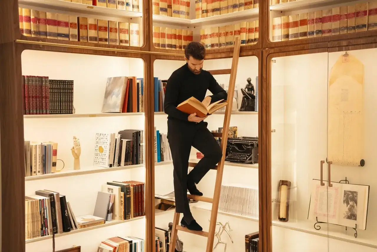 Un hombre en una biblioteca lee un libro, rodeado de volúmenes que evocan a los escritores madrileños actuales.