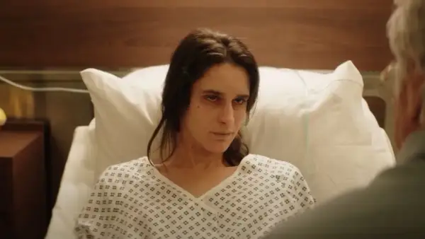 Una mujer en bata de hospital mira fijamente, quizás buscando respuestas sobre el hombre del laberinto final explicado.