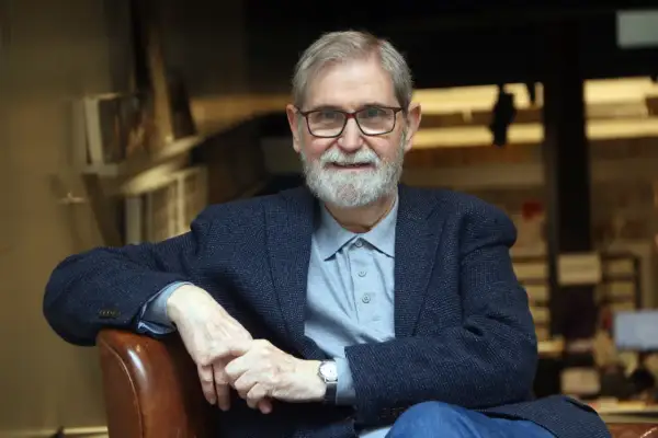 Un hombre mayor con gafas y barba blanca, vestido con chaqueta y polo, evoca la figura de escritores catalanes del siglo XX.
