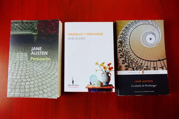 Tres de los mejores libros de Jane Austen: Persuasión, Orgullo y Prejuicio y La abadía de Northanger, dispuestos sobre una mesa de madera.