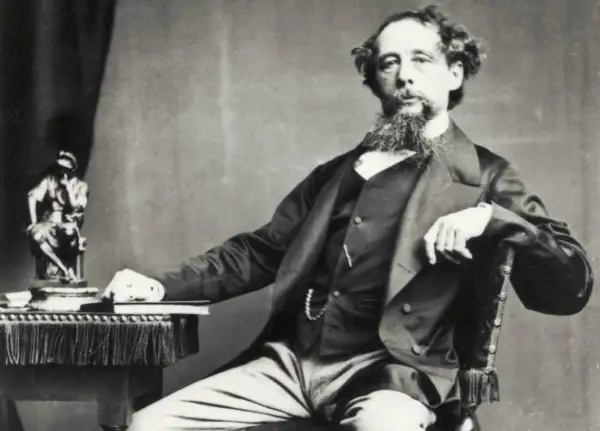 Charles Dickens, autor de libros famosos, posa con una estatua y un libro a su lado.